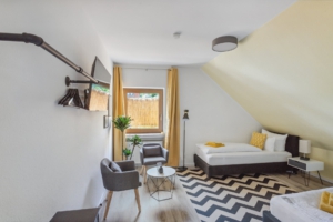 Helles Schlafzimmer mit zwei Einzelbetten, Sitzgruppe, Smart-TV und gelben Akzenten in der Monteurwohnung in Hameln