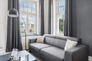 Modern eingerichtetes Wohnzimmer mit gemütlicher Schlafcouch, hohen Fenstern und stilvoller Lampe in der Ferienwohnung in Hameln ‘Juwel in anthrazit’